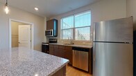 Located at 818 E Long St in Columbus, Ohio, this two-story home showcases a clean, modern design with thoughtfully selected finishes throughout. The main level features an open-concept layout where the living area and kitchen flow seamlessly together. Light hardwood flooring extends across the main floor, complemented by neutral-toned walls and a ceiling fan that enhances the airy feel. Large windows allow generous natural light to fill the living space, which offers views of the surrounding Columbus cityscape.

The kitchen is a standout feature, equipped with stainless steel appliances including a refrigerator, range, microwave, and dishwasher. Rich, dark cabinetry provides ample storage, while granite countertops add a polished look. A central island with a contrasting gray base and matching granite surface is illuminated by pendant lighting, making it both functional and visually striking. A window above the sink introduces additional natural light.

Upstairs, carpeted bedrooms offer a comfortable retreat, each with windows framing outdoor views. The bathrooms are finished consistently with granite-topped vanities, dark wood cabinetry, and hardwood flooring, with one bathroom featuring a glass-enclosed shower. The overall ambiance is contemporary and well-appointed throughout.
