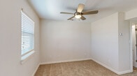 This single-floor unit offers an efficient and thoughtfully designed layout, comprising a living room, kitchen, bathroom, closet, and hallway. The living room serves as the welcoming centerpiece of the space, featuring warm beige carpeting, neutral-toned walls, and a ceiling fan with a built-in light fixture. Multiple windows fitted with horizontal blinds allow natural light to fill the room, creating a bright and airy atmosphere. A hardwood-style entryway transitions seamlessly into the carpeted living area, adding a practical and attractive design detail at the front door. The kitchen is a standout feature, showcasing crisp white shaker-style cabinetry, a classic subway tile backsplash, and a granite-topped peninsula with an undermount sink and a modern pull-down faucet. White appliances, including a refrigerator, electric range, and over-the-range microwave, complement the clean aesthetic, while wood-look flooring ties the space together. The bathroom continues the clean, modern theme with full-height large-format white subway tile surrounding a soaking tub and shower combo, wood-look flooring, and granite countertop detailing. A dedicated closet and hallway provide additional storage and connectivity throughout the unit. Overall, the space presents a cohesive, move-in-ready environment with consistent finishes throughout.