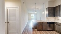 Located along NASA Parkway in Houston, TX, this well-appointed one-bedroom, one-bathroom unit offers a thoughtfully designed single-floor layout. The combined kitchen and living area forms the heart of the home, featuring durable luxury vinyl plank flooring, soaring ceilings, and pendant lighting that adds a modern touch. The kitchen is equipped with dark espresso cabinetry reaching near the ceiling, granite countertops, a tile backsplash, stainless steel appliances including a gas range, built-in microwave, and a French door refrigerator, all centered around a peninsula with a built-in sink. The open living area flows naturally from the kitchen, bathed in natural light. The bedroom is generously sized, finished with plush carpet, a ceiling fan, and large sliding glass doors that open to a private balcony with ornate ironwork railings and lush outdoor views. Two closets provide ample storage, including a spacious walk-in closet outfitted with wire shelving. The bathroom is a standout feature, showcasing floor-to-ceiling marble-style tile, a glass-enclosed walk-in shower, granite vanity countertop, and elegant finishes throughout. A hallway connects the living spaces with clean, neutral tones maintained throughout the unit.