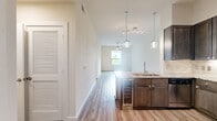 Located along NASA Parkway in Houston, TX, this well-appointed one-bedroom, one-bathroom unit offers a thoughtfully designed single-floor layout. The combined kitchen and living area forms the heart of the home, featuring durable luxury vinyl plank flooring, soaring ceilings, and pendant lighting that adds a modern touch. The kitchen is equipped with dark espresso cabinetry reaching near the ceiling, granite countertops, a tile backsplash, stainless steel appliances including a gas range, built-in microwave, and a French door refrigerator, all centered around a peninsula with a built-in sink. The open living area flows naturally from the kitchen, bathed in natural light. The bedroom is generously sized, finished with plush carpet, a ceiling fan, and large sliding glass doors that open to a private balcony with ornate ironwork railings and lush outdoor views. Two closets provide ample storage, including a spacious walk-in closet outfitted with wire shelving. The bathroom is a standout feature, showcasing floor-to-ceiling marble-style tile, a glass-enclosed walk-in shower, granite vanity countertop, and elegant finishes throughout. A hallway connects the living spaces with clean, neutral tones maintained throughout the unit.
