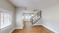 This two-story home combines modern design elements with practical living spaces across two well-proportioned floors. The main level features warm hardwood-style flooring that flows throughout, anchored by a striking staircase with dark wood treads and sleek black cable railings — a standout architectural detail that adds a contemporary touch. The kitchen is a highlight of the home, showcasing white shaker cabinets with matte black hardware, crisp white quartz countertops, a farmhouse sink, stainless steel appliances, and a gray subway tile backsplash that ties the design together cohesively. The full bathroom mirrors this refined aesthetic with gray subway tile surrounding the tub-shower combination and matte black fixtures. The upper level contains the three bedrooms, including a generously sized primary bedroom featuring plush carpeting, multiple windows with white blinds, and ample natural light. The two additional bedrooms are similarly carpeted and well-lit with natural light from windows fitted with plantation-style blinds. Neutral, warm-toned walls throughout the home create a clean, inviting ambiance, while consistent trim work and recessed and flush-mount lighting reinforce the home's cohesive, updated aesthetic.