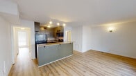 Located at 1613 13th Ave S in Birmingham, Alabama, this single-floor unit offers a practical and well-organized layout suited for comfortable everyday living. The open-concept design connects the living area seamlessly to the kitchen, creating a spacious, airy feel throughout. Light wood laminate flooring runs consistently across the main living spaces, lending warmth and visual continuity to the interior.

The kitchen is thoughtfully designed with gray cabinetry offering ample storage, a tile backsplash, light granite-tone countertops, and a double-basin sink. A peninsula with an overhang extends into the living area, providing additional counter space and casual seating. Black appliances, including a refrigerator, electric range, and over-the-range microwave, complete the kitchen setup. Track lighting illuminates the kitchen area effectively.

The living room is generously proportioned, featuring large windows fitted with horizontal blinds that allow for abundant natural light while maintaining privacy. A wall sconce adds supplemental ambient lighting to the space.

The bedroom is bright and well-lit, with a large window and light wood flooring that mirrors the rest of the unit. A hallway connects the bedroom to the rest of the layout, offering a sense of separation and privacy.

The bathroom features full white square tile on the walls and floors, a soaking tub with shower, and clean, simple fixtures throughout, presenting a functional and tidy space.