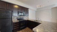 Located at 6667 Wesbury Park Ave in Columbus, Ohio, this single-floor unit offers a well-designed layout with a cohesive blend of modern finishes and practical amenities. The kitchen is a standout feature, showcasing rich dark espresso cabinetry extending to the ceiling, a mosaic tile backsplash, granite-style countertops, and a full suite of black appliances including an electric range, microwave, refrigerator, and double-basin sink. A peninsula counter opens the kitchen to the main living area, which is accented by a bold dark feature wall and plush carpeting throughout. The living space is generously sized and receives good natural light. Multiple bedrooms offer comfortable proportions, each featuring soft carpet flooring, neutral-toned walls, and windows with blinds that allow ample natural light. Two bathrooms serve the unit — one features a walk-in glass-enclosed shower and dark vanity cabinetry with wood-look vinyl flooring, while the second includes a soaking tub/shower combo with a similarly styled vanity. A dedicated in-unit laundry area with a full-size washer and dryer adds everyday convenience. Wood-look vinyl flooring runs through the kitchen and bathroom areas, providing a clean, durable finish throughout.