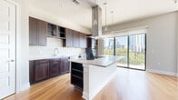 This single-floor residence offers a thoughtfully designed layout highlighted by contemporary finishes and an abundance of natural light. The kitchen serves as a central showpiece, featuring rich dark-wood cabinetry, a white subway tile backsplash, a large center island with a light quartz countertop, and a statement stainless steel range hood suspended above. Pendant lighting and stainless steel appliances, including a double wall oven and refrigerator, complete the space. Floor-to-ceiling windows and sliding glass doors open to a balcony, framing expansive views of the surrounding urban skyline and tree canopy.

The living areas are finished with warm hardwood flooring and neutral-toned walls, creating a clean, modern aesthetic. Bedrooms offer plush carpeting, generous natural light through large windows with city and treetop views, and ceiling fans for comfort. The primary bedroom includes a spacious walk-in closet outfitted with built-in shelving and hanging rods. The primary bathroom presents large-format tile flooring, a soaking tub, a glass-enclosed walk-in shower, and a double vanity with dark cabinetry and a wide framed mirror, delivering a refined, spa-like atmosphere.