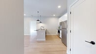 Located at 1000 Sullivans Way in Lake Saint Louis, Missouri, this thoughtfully designed single-floor residence combines modern aesthetics with functional living. Light wood-style flooring flows consistently throughout the space, creating a warm and cohesive feel from room to room.

The open-concept kitchen serves as a central highlight, outfitted with crisp white shaker cabinetry accented by gold hardware, a white subway tile backsplash, dark granite-style countertops, and a full suite of stainless steel appliances including a refrigerator, range, and over-the-range microwave. A center island with a built-in sink and stylish pendant lighting adds both workspace and visual interest, while recessed lighting illuminates the area effectively.

The living area is bright and open, featuring large sliding glass doors with vertical blinds that invite natural light and provide outdoor views. The neutral gray-toned walls offer a clean backdrop adaptable to any décor style.

The bedroom is generously proportioned, featuring large windows that bring in additional natural light and offer views of the surrounding landscape. It connects to what appears to be a walk-in closet, providing ample storage.

The bathroom is well-appointed with a gray vanity, stone-look countertop, white subway tile tub surround, and wood-look flooring, rounding out this clean, contemporary residence.