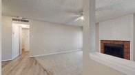 This single-floor residence offers a practical and comfortable layout designed for everyday living. The living room serves as the heart of the home, featuring plush carpeting, a textured ceiling, and a ceiling fan with a light fixture. A wood-trimmed fireplace with a tile surround anchors the room, flanked by windows that allow natural light to filter in and a door providing outdoor access. The transition between the living area and entryway is marked by light wood-style flooring.

The kitchen is equipped with warm-toned wood cabinetry, a stainless steel sink, laminate countertops, and a full-size refrigerator, offering a functional space for meal preparation.

The bedroom is generously sized with soft carpeting, a ceiling fan, and a sliding glass door fitted with vertical blinds that opens to an outdoor view of mature trees. A walk-in closet adjacent to the bedroom provides ample storage with dual hanging rails on each side.

The bathroom features a wide vanity with wood cabinetry, a light countertop, an undermount sink, and a large wall mirror that enhances the sense of space. The flooring transitions to light wood-style vinyl, complementing the clean, neutral palette carried throughout the home.