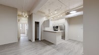 Located at 350 Ionia Ave SW in the heart of Grand Rapids, Michigan, this urban loft-style unit offers a well-designed single-floor layout with an industrial character. The open living and entry area features light wood-look flooring, exposed structural beams, overhead ductwork, and track lighting — all hallmarks of a converted loft aesthetic. Neutral-toned walls and flush ceiling fixtures keep the space feeling bright and clean throughout.

The kitchen is a functional galley-style space outfitted with white shaker cabinetry, light stone-look countertops, a double basin sink, and a full suite of stainless steel appliances including a refrigerator, range, microwave, and dishwasher. A peninsula with bar-height counter extends into the living area, providing additional prep space and a natural divide between the kitchen and main living area.

The bedrooms are carpeted for comfort and feature closets with built-in shelving and hanging rods. One bedroom benefits from large windows with vertical blinds, showcasing painted brick accents that reinforce the loft character of the building. Two bathrooms serve the unit — one with a full soaking tub and shower combination, the other with a walk-in shower stall, both finished with wood-look tile flooring and chrome fixtures.