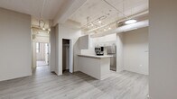 Located at 350 Ionia Ave SW in the heart of Grand Rapids, Michigan, this urban loft-style unit offers a well-designed single-floor layout with an industrial character. The open living and entry area features light wood-look flooring, exposed structural beams, overhead ductwork, and track lighting — all hallmarks of a converted loft aesthetic. Neutral-toned walls and flush ceiling fixtures keep the space feeling bright and clean throughout.

The kitchen is a functional galley-style space outfitted with white shaker cabinetry, light stone-look countertops, a double basin sink, and a full suite of stainless steel appliances including a refrigerator, range, microwave, and dishwasher. A peninsula with bar-height counter extends into the living area, providing additional prep space and a natural divide between the kitchen and main living area.

The bedrooms are carpeted for comfort and feature closets with built-in shelving and hanging rods. One bedroom benefits from large windows with vertical blinds, showcasing painted brick accents that reinforce the loft character of the building. Two bathrooms serve the unit — one with a full soaking tub and shower combination, the other with a walk-in shower stall, both finished with wood-look tile flooring and chrome fixtures.