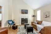 This two-story residence offers a well-organized layout designed for comfortable everyday living. The main level features an open-concept living and dining area anchored by a tiled fireplace and vaulted ceilings that lend a sense of height and openness. Wood-look flooring runs throughout the main living spaces, complemented by natural light from multiple windows. A wall-mounted television above the fireplace and a track lighting system add both function and character to the living area.

The kitchen is efficiently designed with warm oak cabinetry, white countertops, a double-basin stainless steel sink, and a full suite of black appliances including a range, microwave, and dishwasher. A bar-height counter with seating connects the kitchen to the living and dining space, making it ideal for casual meals.

The main level also includes a bedroom with carpeted flooring, a ceiling fan, built-in wall shelving, a walk-in closet, and access to a full bathroom featuring a white vanity and a shower/tub combination.

Upstairs, the primary bedroom is a private retreat with vaulted ceilings, plush carpet, a ceiling fan, and natural light from a window with decorative curtains. An en-suite bathroom with warm yellow accent walls, a well-lit vanity, and a walk-in shower provides added convenience and comfort.