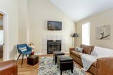This two-story residence offers a well-organized layout designed for comfortable everyday living. The main level features an open-concept living and dining area anchored by a tiled fireplace and vaulted ceilings that lend a sense of height and openness. Wood-look flooring runs throughout the main living spaces, complemented by natural light from multiple windows. A wall-mounted television above the fireplace and a track lighting system add both function and character to the living area.

The kitchen is efficiently designed with warm oak cabinetry, white countertops, a double-basin stainless steel sink, and a full suite of black appliances including a range, microwave, and dishwasher. A bar-height counter with seating connects the kitchen to the living and dining space, making it ideal for casual meals.

The main level also includes a bedroom with carpeted flooring, a ceiling fan, built-in wall shelving, a walk-in closet, and access to a full bathroom featuring a white vanity and a shower/tub combination.

Upstairs, the primary bedroom is a private retreat with vaulted ceilings, plush carpet, a ceiling fan, and natural light from a window with decorative curtains. An en-suite bathroom with warm yellow accent walls, a well-lit vanity, and a walk-in shower provides added convenience and comfort.