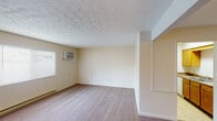 This single-floor residential unit offers a practical and well-organized layout across several distinct living spaces. The main living area is generously sized, featuring wall-to-wall carpeting in a neutral tone and a textured ceiling that adds subtle visual interest. A window unit air conditioner and baseboard heating provide year-round climate control, while blinds on the windows allow for adjustable natural light. The space is bright and open, with cream-colored walls that create a clean, neutral backdrop throughout.

The galley-style kitchen is efficiently designed with warm oak cabinetry lining both sides, offering ample upper and lower storage. Dark laminate countertops provide a contrasting work surface, and the kitchen is equipped with a white electric range, a full-size refrigerator, and a double stainless steel sink. Light tile flooring completes the practical, easy-to-maintain space.

The bedrooms continue the carpeted flooring and textured ceiling aesthetic found throughout the unit, each featuring windows with blinds that allow for natural light while maintaining privacy. Baseboard heaters run along the walls for consistent warmth.

The bathroom is neatly appointed with tile flooring, a single-sink vanity with oak cabinetry, a mirrored medicine cabinet with built-in lighting above, and standard fixtures. The overall unit presents a cohesive, functional design suited for everyday living.