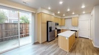 This two-story residence at 5123 Dowdell Ave in Rohnert Park, California, offers a well-designed layout with clean, contemporary finishes throughout. The main level features a thoughtfully appointed kitchen equipped with light maple cabinetry, white quartz countertops, stainless steel appliances including a gas range, built-in microwave, and French door refrigerator, plus a central island providing additional workspace. Wood-look flooring runs through the main level, lending warmth and cohesion. A sliding glass door in the kitchen opens to a private outdoor patio, allowing natural light to fill the space. A convenient half bath on this level features wood-look flooring, a pedestal sink, and a round mirror. The staircase leads to the upper floor, where carpeted bedrooms offer a comfortable retreat. The primary bedroom is generously proportioned with multiple windows framing views of surrounding greenery. The upper-level bathroom includes a wide vanity with ample cabinetry and a well-lit mirror. A dedicated laundry room with light maple cabinetry, countertop space, and a natural light window adds everyday convenience. Additional rooms with wood-look flooring and recessed lighting provide flexible living or workspace options throughout.