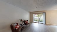This single-floor residence offers a thoughtfully organized layout designed for comfortable everyday living. The living area is bright and welcoming, featuring light-toned laminate wood flooring, neutral warm walls, and a textured ceiling. Large sliding glass doors open to a private balcony overlooking lush greenery and mature trees, allowing generous natural light to fill the space. A ceiling fan and an additional window further enhance ventilation and brightness in this area.

The galley-style kitchen is efficiently designed with white cabinetry extending to the ceiling, dark countertops, and stainless steel appliances including a gas range, microwave, and refrigerator. Light wood-style flooring continues throughout, giving the kitchen a clean and cohesive look.

The bedroom is a calm retreat with plush wall-to-wall carpeting, a window with outdoor views, and ample space for furnishings. Conveniently tucked nearby is an in-unit laundry area featuring a stacked washer and dryer unit, alongside a vanity with white cabinetry and a well-lit mirror — providing practical functionality within easy reach.

Throughout the space, the consistent use of neutral tones, clean finishes, and an abundance of natural light creates a bright, airy, and inviting atmosphere.