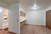 Located at 1082 E Chicago Blvd in Tecumseh, MI, this single-floor, one-bedroom, one-bathroom unit offers a functional and straightforward layout across a compact but efficient footprint. The living room is the centerpiece of the space, featuring wall-to-wall carpet, a textured ceiling, and a full-length sliding glass door with vertical blinds that floods the room with natural light and provides views of the lush greenery beyond. A wall-mounted air conditioning unit and baseboard heating ensure year-round comfort. The kitchen is accessed via a pass-through counter with wood-laminate cabinetry above and below, offering a practical open connection to the dining area. Inside the kitchen, a range, refrigerator, and sink are neatly arranged with upper cabinetry for additional storage. The bedroom is a well-sized, carpeted retreat with two wood-paneled closet doors, offering generous storage options. A hallway connects the main living areas to the full bathroom, which features a clean, white tub/shower combination with a curtain rod and baseboard heating. Throughout the unit, neutral white walls, carpeted floors, and consistent baseboard heating create a cohesive, low-maintenance living environment.