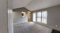 This single-story, 2-bedroom, 1-bathroom residence offers a well-organized layout across a comfortable footprint. The living room serves as the heart of the home, showcasing vaulted ceilings that lend a sense of openness and height, soft carpet flooring, and a striking black-tiled fireplace. Large windows and a sliding glass door with vertical blinds flood the space with natural light while providing outdoor access. A pass-through window connects the living area to the kitchen, which features wood cabinetry, a pantry, and easy flow into the adjacent dining room. The dining area continues the warm, functional aesthetic with wood-style flooring. Both bedrooms are carpeted and neutrally toned; the primary bedroom offers a comfortable footprint with natural light from a window with vertical blinds and a ceiling fan, while the second bedroom is similarly appointed with carpet and ample wall space. Three closets throughout provide generous storage. The shared bathroom is well-appointed with a dark wood vanity, granite-style countertop, wood-look flooring, and a tub-shower combination with marble-style tile surround. A dedicated laundry area and hallway round out the layout, making this a complete and practical living space.