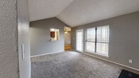 This single-story, 2-bedroom, 1-bathroom residence offers a well-organized layout across a comfortable footprint. The living room serves as the heart of the home, showcasing vaulted ceilings that lend a sense of openness and height, soft carpet flooring, and a striking black-tiled fireplace. Large windows and a sliding glass door with vertical blinds flood the space with natural light while providing outdoor access. A pass-through window connects the living area to the kitchen, which features wood cabinetry, a pantry, and easy flow into the adjacent dining room. The dining area continues the warm, functional aesthetic with wood-style flooring. Both bedrooms are carpeted and neutrally toned; the primary bedroom offers a comfortable footprint with natural light from a window with vertical blinds and a ceiling fan, while the second bedroom is similarly appointed with carpet and ample wall space. Three closets throughout provide generous storage. The shared bathroom is well-appointed with a dark wood vanity, granite-style countertop, wood-look flooring, and a tub-shower combination with marble-style tile surround. A dedicated laundry area and hallway round out the layout, making this a complete and practical living space.