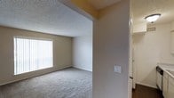 This 1-bedroom, 1-bathroom single-floor unit is a well-proportioned residence offering an efficient and comfortable layout. The living area features soft wall-to-wall carpeting underfoot, creating a warm and inviting atmosphere. A large window dressed with vertical blinds allows natural light to fill the space, brightening the neutral-toned walls and contributing to an open, airy feel. The textured ceiling adds a classic architectural touch consistent throughout the unit. The open passageway connecting the entry corridor to the main living area enhances the sense of flow between spaces. Neutral beige and warm gray tones are carried throughout the interior, providing a versatile backdrop ready for personalization. The layout is intelligently designed to make the most of the available space, with clearly defined living zones that balance function and comfort. Additional features include wall-mounted light switches and easy access to adjacent rooms. This unit is ideal for individuals or couples seeking a manageable, well-lit living space with a practical, no-frills design that prioritizes everyday functionality.