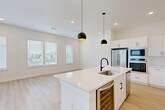 Located at 33200 Forest West St in Magnolia, TX, this two-story home offers a clean, modern aesthetic across two well-appointed floors. The ground level houses an attached garage with an automatic opener, providing secure parking and additional storage space. The main living floor features an open-concept layout that seamlessly connects the dining room, kitchen, and living room. The kitchen is a standout, boasting white flat-front cabinetry with matte black hardware, a large center island with a built-in sink, quartz countertops, stainless steel appliances including a double wall oven and French door refrigerator, a wine cooler, a sleek electric cooktop, and a white subway tile backsplash. Stylish pendant lights with black globe shades illuminate the island, while recessed lighting and multiple windows fill the space with natural light. Light hardwood-style flooring runs throughout the main living areas. A powder bathroom on this level features decorative patterned tile flooring and a pedestal sink. Upstairs, two carpeted bedrooms offer bright, comfortable retreats with ample natural light through large windows. The primary bedroom includes a walk-in closet with built-in shelving. Three bathrooms in total serve the home. Ceiling fans, recessed lighting, and a neutral color palette complete the bright, contemporary ambiance throughout.