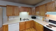 This single-floor residence offers a practical and well-organized layout across multiple rooms, all unified by warm-toned hardwood-style flooring and neutral white walls that create a clean, cohesive aesthetic throughout. Textured ceilings and wood-trimmed windows are consistent design elements found in each room, lending a modest but cohesive character to the space.

The kitchen is equipped with an abundance of oak cabinetry providing generous storage, light-colored countertops, a double-basin stainless steel sink, a dishwasher, and an electric range. A wide window in the adjoining area allows natural light to flow into the space, which opens toward a small living area.

Multiple bedrooms are present, each featuring wood-trimmed windows that overlook the surrounding neighborhood and greenery, flush-mount ceiling light fixtures, and ample floor space suitable for various furniture arrangements. The rooms share a consistent, understated design that prioritizes functionality.

Two full bathrooms serve the unit, each featuring a tub-shower combination with curtain, a vanity with storage, a mirror, and tile flooring. The bathrooms are straightforward in design with clean, white fixtures throughout.

Overall, the space presents a functional and neutral environment well-suited for comfortable everyday living.