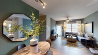 This single-floor residence offers a thoughtfully designed layout with modern finishes and a cohesive color palette throughout. The open-concept living and dining area is a standout feature, with bold green accent walls, track lighting, and wood-look flooring that carry a contemporary aesthetic. The living room is bright and welcoming, featuring a ceiling fan, large windows with blinds that allow generous natural light, and direct access to an exterior door. The adjacent dining area accommodates a round wood table with modern chairs and is accented by a large octagonal mirror and decorative wall art, adding personality to the space. The kitchen is well-appointed with dark espresso cabinetry, granite-style countertops, stainless steel appliances, and a peninsula with bar seating — ideal for casual dining or entertaining. Two bedrooms provide comfortable retreats; one features cool blue-gray tones with a ceiling fan, while the other offers a softer, neutral palette with a workspace and ample natural light. Both bathrooms are finished with dark vanity cabinetry, granite countertops, and wood-look flooring. The full bathroom includes a tub-shower combination with tile surround. Overall, the space presents a stylish and functional environment with consistent, modern design elements throughout.