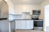 Located at 1200 Talwood Dr in Peterborough, Ontario, this well-appointed one-bedroom, one-bathroom unit offers a clean, modern aesthetic throughout its efficiently designed layout. Light-toned hardwood-style flooring runs continuously across all rooms, lending a cohesive and airy feel to the entire space.

The living room is the standout area of the unit, featuring a large floor-to-ceiling sliding window that draws in abundant natural light and provides open outdoor views, creating a bright and inviting atmosphere. Baseboard heating runs along the perimeter, and crisp white walls complement the light flooring throughout.

The kitchen is thoughtfully designed with white cabinetry, classic white subway tile backsplash, and stainless steel appliances including a range and microwave. It opens conveniently toward the living area, allowing for a functional and connected flow between spaces.

The bedroom is a comfortable, well-sized room featuring a closet and the same warm flooring found throughout. Its clean white walls and simple layout make it a versatile and restful retreat.

The bathroom is finished with full white subway tile surrounding the soaker tub and shower combination, paired with chrome fixtures for a polished, timeless look.

A hallway connects all areas of the unit seamlessly. The overall ambiance is clean, bright, and move-in ready, reflecting a modern and practical residential design.