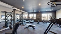 This fitness center at 340 S Market St in Wilmington, Delaware, offers a well-appointed workout space designed to accommodate a full range of exercise needs. The interior features a dark, graphite-toned ceiling with recessed lighting and an exposed ventilation system, lending the space an industrial-modern aesthetic. Multi-toned, patterned carpet tiles cover the floors throughout, providing durability and a contemporary look.

The space is divided into distinct functional zones. The cardio area lines one side of the room with a row of Matrix treadmills, an elliptical trainer, and a stair climber, positioned near large windows that allow natural light and views of the surrounding streetscape. A motivational "Harder. Better. Faster. Stronger." wall graphic energizes this section. The strength training area features a functional cable machine, a vertical knee raise station, an adjustable weight bench, and a full dumbbell rack displayed in front of floor-to-ceiling mirrors that enhance the sense of space. A wall-mounted flat-screen television adds convenience for entertainment during workouts. Near the entry, a water fountain station and ceiling fan complete the practical amenities, ensuring a comfortable and fully equipped fitness experience.