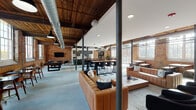 This thoughtfully reimagined industrial space in South Carolina masterfully blends historic character with modern functionality. The single-floor layout retains its original exposed brick walls, warm wood-beam ceilings, and polished concrete floors throughout, creating a cohesive industrial-chic aesthetic that anchors every zone of the interior.

The expansive open-plan layout is defined by steel support columns and deliberately zoned into distinct areas. A generous lounge area features plush tan leather sofas arranged around a central coffee table, while a dedicated recreation corner includes a billiard table and wall-mounted television set against raw brick. A comfortable leather lounge chair and side tables create an intimate retreat in one brick-walled nook.

The dining and social areas are well-appointed, offering a mix of long communal tables with bench seating and taller bar-height tables with modern chairs. Large multi-pane industrial windows line the perimeter, flooding the space with abundant natural light and providing views of the surrounding neighborhood.

A fully equipped kitchen features dark cabinetry with brushed gold hardware, white countertops, stainless steel appliances, and a large island. Exposed ductwork and pendant lighting reinforce the industrial character throughout, while the open ceiling structure adds a sense of generous vertical volume to the entire space.