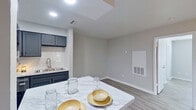 This well-appointed single-floor unit offers a clean, modern aesthetic throughout, highlighted by light wood-style luxury vinyl flooring and a neutral gray color palette that creates a bright, cohesive atmosphere. The open-concept layout greets you at the entry with an airy living area that flows directly into a fully equipped kitchen. The kitchen is a standout feature, showcasing dark charcoal cabinetry contrasted by marble-look countertops, a subway tile backsplash, stainless steel appliances including a refrigerator, range, and microwave, and a peninsula that doubles as a casual dining surface. Recessed lighting overhead keeps the kitchen bright and functional. The dining area adjacent to the kitchen provides a comfortable gathering space. The bedroom is generously sized, featuring dual windows that fill the room with natural light and a ceiling fan for comfort. A sliding glass door in a secondary room or flex space opens directly to an outdoor patio, extending the living area outside. The bathroom is updated with a marble-look vanity top, dark cabinetry, a framed mirror, and brushed nickel fixtures. Throughout the unit, clean white baseboards and modern recessed lighting reinforce the polished, move-in-ready feel of this thoughtfully renovated space.