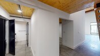 Located at 701 Easley Bridge Rd in Greenville, SC, this two-story space masterfully combines industrial architecture with contemporary design elements. The main level immediately impresses with soaring ceilings, polished concrete floors, and generous natural light streaming through large black-framed windows and a glass door. Pendant lighting fixtures hang from the dramatic ceiling height, while a wood-and-steel staircase anchors the open floor plan and leads to the upper level.

The kitchen is outfitted with white cabinetry featuring matte black hardware, dark granite countertops, stainless steel appliances, and a distinctive penny-tile backsplash. A bathroom on this level features a white undermount sink set into dark granite, white cabinetry, and coordinating matte black fixtures and hardware throughout.

The upper level reveals warm natural pine hardwood flooring and richly toned exposed wood beam ceilings with visible ductwork, reinforcing the industrial aesthetic. This floor includes an open loft-style room with a ceiling fan, a bathroom with light pine flooring and matching black hardware, and a walk-in closet area. Throughout both floors, crisp white walls contrast beautifully with the warm wood and dark metal accents, creating a cohesive, modern-industrial ambiance.