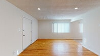 This single-floor unit presents a well-organized layout with a consistent design language throughout. The main living area is generously proportioned, featuring warm-toned hardwood flooring that extends across the space, crisp white walls, and a textured ceiling with recessed lighting that provides even, practical illumination. A window dressed with vertical blinds allows natural light to filter into the room, enhancing its open and airy feel.

An additional room, accessible via an open doorway from the living area, mirrors the same hardwood flooring and neutral wall tones. It includes a window with vertical blinds, a flush-mount ceiling fixture, and clean baseboards throughout, making it a versatile space suitable for various uses.

The galley-style kitchen is efficiently designed, featuring warm honey-toned wood cabinetry extending to the ceiling for ample storage, bold granite countertops with contrasting dark veining, and tile flooring. White appliances, including a gas range, dishwasher, refrigerator, and over-the-range microwave, are neatly integrated into the layout.

The bathroom is finished with tile flooring, a granite-topped vanity with wood cabinetry, and a bathtub and shower combination enclosed by sliding glass doors, completing the unit's functional and cohesive interior.