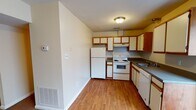Located at 5112 Skyway Ct in Sandston, Virginia, this two-floor home offers a straightforward and functional layout across both levels. The kitchen is equipped with wood-trimmed cabinetry in a combination of white and warm wood tones, dark countertops, and white appliances including a refrigerator, electric range, and dishwasher. Hardwood-style flooring runs throughout the kitchen, which also features sliding vertical blinds offering access to an adjacent area.

The main living area is generously sized, featuring neutral carpet and a large front-facing window that allows natural light to fill the space. The open layout connects seamlessly to additional rooms, providing a comfortable flow throughout the first floor.

Upstairs, the bedrooms are carpeted and neutrally painted, each with windows that bring in natural light and views of the surrounding greenery. One bedroom includes a double closet. A full bathroom with a tub-shower combination and a clean, simple design serves the upper level. A dedicated laundry closet on the upper floor houses a stacked washer and dryer unit, adding everyday convenience. Throughout, the home maintains a clean and practical aesthetic.