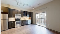 Located in the vibrant East Nashville neighborhood, this one-bedroom, one-bathroom unit at 120 South 5th Street offers a thoughtfully designed layout that maximizes every inch of its compact footprint. Light-toned hardwood-style flooring flows throughout the main living and kitchen areas, creating a cohesive and contemporary aesthetic.

The open kitchen is a standout feature, outfitted with dark espresso cabinetry, light countertops, a classic white subway tile backsplash, and a full suite of stainless steel appliances including a range, microwave, dishwasher, and refrigerator. Track lighting overhead adds a modern touch and ensures the space is well-lit. A sliding glass door leads directly to a private balcony, bringing in natural light and offering views of the surrounding Nashville cityscape.

The bedroom is a quiet retreat with plush wall-to-wall carpeting and a large window fitted with blinds. It features direct access to both a dedicated walk-in closet with built-in wire shelving and the full bathroom. The bathroom is clean and functional, featuring a soaking tub and shower combination with white tile surround and brushed nickel fixtures. The walk-in closet provides practical storage with multi-level shelving throughout.