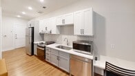 This studio in Austin, TX offers a thoughtfully designed single-floor layout that maximizes functionality within a compact footprint. The main living area features warm wood-look flooring, crisp white walls, and a ceiling fan with integrated lighting, creating a bright and comfortable atmosphere. Two windows fitted with horizontal blinds allow natural light to fill the space while providing privacy. The living area comfortably accommodates a bed with built-in storage drawers, a sofa, a wall-mounted television, and a dedicated desk workspace, making it well-suited for both relaxing and studying. A reach-in closet with double rods provides convenient storage directly off the living area. The kitchen is efficiently designed with a galley-style layout, featuring white shaker upper cabinets, contrasting lower cabinetry, white quartz countertops, and a subtle tile backsplash. Stainless steel appliances include a gas range, dishwasher, refrigerator, and microwave, offering a fully equipped cooking setup. The bathroom continues the clean aesthetic with wood-look flooring, a tub-shower combination featuring gray tile surround, and a vanity with mirror. Throughout the space, consistent finishes and a neutral color palette contribute to a cohesive, modern feel.
