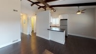 This single-floor, one-bedroom, one-bathroom unit combines architectural character with functional design. The living area is defined by striking exposed dark wood beam ceilings that add warmth and visual interest to the otherwise neutral, light-toned walls. Large windows fitted with vertical blinds allow natural light to fill the space, highlighting the rich, dark hardwood flooring that runs throughout the main areas.

The kitchen is designed for efficiency, featuring a galley-style layout with white shaker cabinetry, dark countertops, a white subway tile backsplash, and a full suite of stainless steel appliances including a gas range with overhead microwave and a full-sized refrigerator. A peninsula with a dark countertop provides a convenient transition between the kitchen and the open living area.

The bedroom is carpeted for comfort and benefits from natural light through a side window. A mirrored sliding-door closet provides generous storage while visually expanding the room.

The bathroom maintains a clean, modern aesthetic with white cabinetry, dark countertops, wood-look flooring, an undermount sink, and a shower-tub combination, creating a cohesive and polished finish throughout the unit.