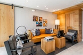 This thoughtfully designed single-floor space blends contemporary aesthetics with warm, natural materials throughout. The open-concept kitchen is a standout feature, showcasing a striking marble waterfall island with leather-upholstered bar stools, dark wood cabinetry, and a distinctive ceiling detail of wood slat beams adorned with globe pendant lights. Adjacent to the kitchen, a bright dining area with a round table and modern chairs is separated by a sleek glass partition, adding openness while maintaining definition between spaces.

The lounge area exudes a curated, artistic character, anchored by a rich amber sofa accented with blue and mixed-pattern throw pillows. Solid wood cube coffee tables serve as both functional and decorative elements, while a gallery wall of colorful jazz-themed art prints adds cultural personality. A wall-mounted fireplace with a built-in media center and floor-to-ceiling windows draw the eye toward an outdoor balcony, offering expansive views of the surrounding cityscape and landscape.

Natural light pours through the large sliding glass doors, seamlessly connecting the interior to the balcony. Warm wood accent walls, a sliding barn door, and light-toned large-format tile flooring provide cohesion throughout. The accessible bathroom features dark stone tile walls, chrome grab bars, and clean, minimal fixtures, reflecting both function and design precision. Recessed lighting throughout enhances the space's modern and welcoming ambiance.
