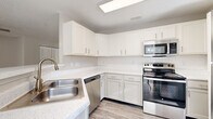 Located at 220 Indian Park Drive in Murfreesboro, Tennessee, this five-bedroom, two-bathroom home offers a well-organized layout across a single floor. The kitchen is appointed with white shaker cabinetry, quartz-style countertops, a white subway tile backsplash, and a full suite of stainless steel appliances including a range, over-the-range microwave, dishwasher, and refrigerator. Light wood-look flooring runs through the kitchen and common areas, lending a clean, cohesive aesthetic throughout. The sun-filled dining area features large windows fitted with horizontal blinds and an elegant chandelier overhead, allowing natural light to pour in generously. The living room provides direct outdoor access through a glass-panel door alongside additional windows, enhancing the bright and airy feel of the space. Five bedrooms offer plush carpeting, ceiling fans, and windows with exterior views. The primary bedroom includes a dedicated walk-in closet with wire shelving. Two bathrooms feature wood-look flooring, vanities with under-sink storage, and tub-shower combinations. The laundry room includes a washer and dryer, wire shelving, and a charming octagonal window. Carpeted staircases with white railings connect the levels of the home.