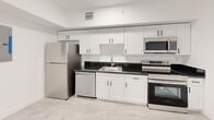 Located at 147 NW 59th St, Unit 301 in Miami's vibrant 33127 zip code, this unit offers four bedrooms and two bathrooms across a single floor. The layout is efficiently organized, with a connecting hallway linking all rooms in a clean, functional flow. The kitchen is a standout feature, equipped with stainless steel appliances including a refrigerator, dishwasher, range, and built-in microwave. White shaker-style cabinetry with dark hardware pairs with dark granite countertops, creating a modern contrast. Light-toned tile flooring runs throughout the main areas, contributing to a bright and cohesive aesthetic. Each bedroom is finished with crisp white walls and benefits from natural light through windows, with several rooms offering closet space. The bedrooms maintain a clean, neutral palette that provides versatility for various uses. Both bathrooms are identically appointed with large-format dark gray tile surround showers featuring hexagonal white mosaic tile floors and chrome fixtures — a sharp, contemporary design choice. The overall interior aesthetic is modern and minimalist, with a consistent white finish throughout that maximizes the sense of space and light within this well-appointed Miami unit.