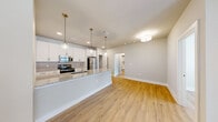 This well-designed 2-bedroom, 1-bathroom single-floor unit offers a thoughtful layout with modern finishes throughout. The open-concept kitchen and living area serves as the heart of the home, featuring crisp white shaker cabinetry, granite countertops, a subway tile backsplash, and a full suite of stainless steel appliances including a refrigerator, electric range, and microwave. Pendant lighting over the kitchen island adds a stylish touch, complementing the flush-mount fixtures in the living area. Light hardwood-style flooring runs seamlessly throughout the entire unit, creating a cohesive and bright aesthetic. The living area includes a ceiling fan with integrated lighting and access to a private exterior door with a sidelight window, allowing natural light to fill the space. Both bedrooms are comfortably sized, each equipped with ceiling fans and windows with exterior views. The bathroom is finished with marble-style tile surrounding the tub and shower, a granite-topped vanity, white cabinetry, and brushed nickel fixtures. Additional highlights include a dedicated laundry area with a washer and dryer, a spacious walk-in closet with wire shelving, and a hallway connecting all rooms efficiently. A large pantry/storage closet adjacent to the kitchen provides ample additional storage.