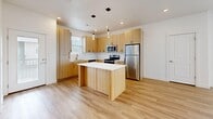 This three-bedroom, two-and-a-half-bathroom home in Ogden, Utah is spread across three floors, offering a well-organized layout designed for comfortable living. The ground floor features an entrance that leads into the main living level, where an open-concept kitchen and living room serve as the heart of the home. The kitchen is a standout space, outfitted with light wood cabinetry, white quartz countertops, a central island with pendant lighting, stainless steel appliances, and light hardwood flooring — all contributing to a clean, contemporary aesthetic. The living area flows naturally from the kitchen, bathed in natural light from multiple windows. A convenient half-bath on the main level features matching warm wood vanity cabinetry and light hardwood floors. The upper floor hosts all three bedrooms, including a primary bedroom with a double-door closet and plush carpeting. The secondary bedrooms are bright and airy, each featuring large windows with views of the surrounding neighborhood and mountain scenery. The full bathrooms are finished with white surrounds, warm wood vanities, and hardwood-style flooring. Throughout the home, the consistent use of light tones, recessed lighting, and quality finishes create a cohesive and inviting atmosphere.