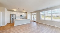 Located at 1774 W Orchard Rd in North Aurora, Illinois, this single-floor home showcases a thoughtfully designed open-concept layout with a bright, welcoming ambiance throughout. The main living area features light-toned luxury vinyl plank flooring, neutral warm-beige walls, and abundant natural light streaming through large windows and a transom-topped double entry door, creating an airy and inviting atmosphere with outdoor views.

The kitchen is a standout feature, offering a two-tone cabinetry design with crisp white upper cabinets and soft blue-gray lower cabinets, all complemented by white countertops. A central island with pendant lighting provides additional workspace and casual seating. Stainless steel appliances, including a French door refrigerator, built-in microwave, and electric range, complete this functional and stylish space. A secondary door with transom window provides direct outdoor access from the kitchen area.

The bedrooms are carpeted for comfort, featuring neutral tones, ample natural light from well-placed windows, and generous closet space with built-in shelving. The bathrooms, as seen in the floor plan, include walk-in shower configurations. The home's single-floor design ensures seamless flow between all spaces, making it an accessible and practical living environment.