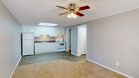 Located at 2100 Apalachee Pkwy in Tallahassee, FL, this single-story, one-bedroom, one-bathroom unit offers a practical and efficiently designed layout across a compact footprint. The interior features a neutral color palette of warm grays and whites throughout, complemented by white trim and textured ceilings.

The kitchen is a standout area, equipped with white cabinetry extending to the ceiling, dark granite-style countertops, a stainless steel sink, and white appliances including a refrigerator and electric range. A recessed skylight panel overhead provides bright, even lighting, and wood-look plank flooring ties the kitchen into the open adjacent living area seamlessly.

The bedroom is a comfortable, carpeted space featuring a ceiling fan with light fixture and a window that allows natural light and outdoor views of surrounding greenery. A full-width bi-fold closet provides ample storage along one wall, while the textured ceiling and crown molding add a finishing detail.

The bathroom includes a white vanity with storage, a wall mirror, wood-look flooring, and a full tub-shower combination. A utility room and hallway complete the layout, contributing to the unit's organized and functional flow throughout.