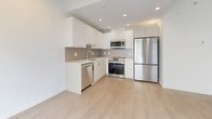 Located at 520 1st St E in North Vancouver, BC, this well-appointed one-bedroom, one-bathroom unit offers a clean, contemporary design with a bright and efficient layout. Light-toned engineered hardwood flooring runs throughout, complementing the crisp white walls and modern finishes that give the space a fresh, airy feel.

The open-concept kitchen and living area serves as the heart of the unit, featuring flat-front white cabinetry extending to the ceiling, a tile backsplash, light countertops, and a full suite of stainless steel appliances including a refrigerator, electric range, built-in microwave, and dishwasher. Recessed lighting illuminates the space efficiently.

A bright hallway connects the main living area to the private quarters, with the bathroom accessible along the way. The bathroom is finished in crisp white tile and includes a deep soaker tub with chrome fixtures. A dedicated laundry area and two closets provide practical storage solutions.

The bedroom is a well-proportioned, sunlit room featuring a window with views of the surrounding building exterior and access to a walk-in closet with built-in shelving. A private balcony extends the living space outdoors. The overall design is cohesive, minimal, and functional — well-suited for modern urban living in North Vancouver.
