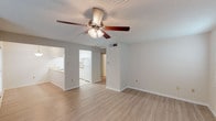 This single-story, one-bedroom, one-bathroom unit features a thoughtfully organized layout that maximizes its comfortable footprint. The open living area is finished with light wood-style hard-surface flooring and neutral gray walls, creating a bright and airy atmosphere. A ceiling fan with integrated lighting serves as a central fixture, enhancing both air circulation and illumination. Multiple windows fitted with horizontal blinds allow natural light to filter through, contributing to the welcoming feel of the space.

The galley-style kitchen is efficiently arranged with white cabinetry lining both walls, offering ample upper and lower storage. Light-toned countertops, tile flooring, a white electric range, dishwasher, and a stainless steel sink complete the kitchen's functional design.

The bedroom is carpeted for added comfort and includes two windows that bring in natural light, along with its own ceiling fan with lighting. The full bathroom features tile flooring, a tub-shower combination with tiled surround, a toilet, and a grab bar for added accessibility. A textured ceiling finish appears throughout the unit, adding a consistent design element across all rooms.