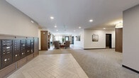 Located at 4021 Coon Rapids Blvd NW in Coon Rapids, Minnesota, this thoughtfully designed common area serves as a central hub for residents. The space is organized across a single floor and encompasses a welcoming lobby entrance, a comfortable lounge area, and a dedicated fitness center.

The lobby greets visitors with herringbone-patterned tile flooring that transitions seamlessly into plush carpeting throughout the rest of the space. A bank of mailboxes with warm wood cabinetry lines one wall, while framed artwork adds a polished, residential feel to the corridors. Black-framed glass doors provide secure entry points and allow natural light to filter in from the exterior.

The lounge area is a standout feature, designed with a mid-century modern aesthetic. Rich wood wall paneling frames a marble-surround fireplace flanked by built-in shelving. Comfortable seating and a round dining table beneath a sculptural globe chandelier create a refined yet inviting atmosphere, with large windows offering views of the surrounding neighborhood.

The fitness center is generously proportioned and well-lit by large windows overlooking greenery outdoors. It is equipped with treadmills, an elliptical, a multi-station cable machine, free weights, and a water fountain station. Neutral carpet and recessed lighting maintain a clean, functional environment throughout.
