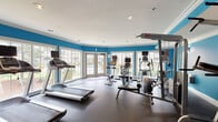 The fitness center at 4306 N Shallowford Rd in Chamblee, Georgia, is a well-equipped, single-floor facility designed to support a comprehensive workout experience. The interior is defined by bold blue accent walls contrasted with crisp white crown molding and ceilings, creating an energetic and motivating atmosphere. Recessed lighting throughout ensures consistent illumination across the entire space.

The cardio zone is a highlight of the facility, featuring multiple treadmills and an elliptical trainer positioned along a wall of large windows and glass doors that offer direct views of an outdoor pool area. This natural light-filled section provides an inviting environment for aerobic exercise.

The strength training area is equally well-appointed, housing several Quantum cable machines and multi-functional weight stations suitable for a wide range of resistance exercises. A dedicated free weights section includes a tiered dumbbell rack, weight benches, and a stability ball, offering versatility for both beginner and advanced users.

A separate section of the facility accommodates additional accessories, including yoga mats, foam rollers, and a mini trampoline, supporting flexibility and functional fitness routines. Full-length mirrors along one wall enhance the sense of space and allow users to monitor their form during workouts. The durable rubberized flooring throughout provides safety and comfort during all types of exercise.