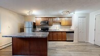 Located at 548 E Summit St in Kent, Ohio, this single-floor unit offers three bedrooms and one full bathroom within a compact, efficiently arranged floor plan. The kitchen is a standout feature, showcasing rich warm-toned cabinetry, granite-style countertops, and a full suite of stainless steel appliances including a refrigerator, electric range, built-in microwave, and dishwasher. A central kitchen island provides additional prep and dining space, and track lighting throughout the kitchen ensures excellent illumination. The kitchen opens directly into the living area, which features light wood-style flooring and a window that brings in natural light. The living space transitions to carpet, creating a comfortable, defined zone. Each of the three bedrooms is carpeted and features neutral walls and closets with built-in hanging rods for storage. The full bathroom includes a single-sink vanity with wood cabinetry, a tub-shower combination, tile accents, and mosaic tile flooring. Baseboard heating is present throughout the unit. A hallway connects the main living spaces to the bedrooms and bathroom, contributing to an organized and functional layout.
