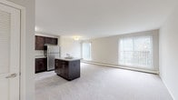 Located at 300 E Marshall St in Pennsylvania, this single-floor residence offers a well-designed, functional layout that balances comfort and practicality. The open-concept living and kitchen area serves as the heart of the home, where a generously sized living space flows seamlessly into a fully equipped kitchen. The kitchen is outfitted with rich, dark-stained cabinetry offering ample storage, granite-style countertops, a central island, and a full suite of stainless steel appliances including a refrigerator, electric range, microwave, and dishwasher. Light tile flooring in the kitchen complements the neutral tones throughout the space. Large windows in the living area admit abundant natural light and frame views of surrounding greenery, creating a bright and airy atmosphere. The bedrooms are carpeted and generously proportioned, each featuring baseboard heating and access to natural light. The bathrooms are clean and functional, featuring white vanities with under-sink storage, mirrored medicine cabinets, and tiled floors. One bathroom includes a shower-tub combination. Soft, neutral wall tones and plush carpeting throughout the living and sleeping areas contribute to a calm, welcoming ambiance. The overall layout, as seen in the dollhouse view, provides a practical flow between all areas of the home.