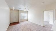 Located in Pflugerville, TX, this single-story, 3-bedroom, 2-bathroom home offers a comfortable and functional layout designed for everyday living. The open-concept living, dining, and kitchen area forms the heart of the home, with plush carpeting underfoot and a ceiling fan overhead. A hard-surface entryway transitions seamlessly into the carpeted living space, which is brightened by a large window with vertical blinds. The kitchen features a peninsula-style breakfast bar, yellow cabinetry, and a white appliance suite, making it both practical and accessible from the main living and dining areas. Each of the three bedrooms is carpeted and equipped with a ceiling fan. The generously sized primary bedroom benefits from two windows that invite abundant natural light and views of the surrounding greenery. Each bedroom includes a dedicated closet, with wire shelving systems providing organized storage. The two bathrooms are finished with tiled tub-and-shower combos featuring a classic white and tan checkerboard accent border, complemented by wood-look flooring. Additional highlights include an in-unit laundry area, a utility room, and three closets throughout, ensuring ample storage. The neutral color palette and clean lines create a bright, move-in-ready atmosphere throughout the home.