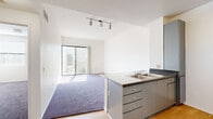 Located at 510 E Third St in Pomona, CA, this two-bedroom, two-bathroom unit offers a thoughtfully designed single-floor layout with a clean, modern aesthetic throughout. The open-concept kitchen and living area serve as the heart of the home, where light wood-style flooring flows underfoot and a track lighting fixture illuminates the space. The kitchen features gray cabinetry, dark granite-style countertops, a double-basin stainless steel sink, and a full suite of stainless steel appliances including a refrigerator, range, and built-in microwave. A peninsula connects the kitchen to the living area, which is finished with plush purple-toned carpet and a sliding glass door that fills the room with natural light and provides access to an outdoor balcony with views of the surrounding neighborhood. Both bedrooms are carpeted, bright, and well-proportioned, each featuring sliding closets and windows with blinds. The primary bathroom stands out with an L-shaped double-vanity topped with dark granite counters, gray cabinetry, wood-style flooring, and large mirrors with Hollywood-style lighting. The second bathroom offers a full tub and shower combo with wood-style flooring and crisp white walls. Three closets provide ample storage throughout the unit.