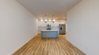 This well-designed two-story home offers a thoughtful layout with modern finishes throughout. The kitchen serves as a central highlight, featuring white shaker-style cabinetry extending to the ceiling, light quartz countertops, stainless steel appliances including a refrigerator with ice dispenser, electric range, and built-in microwave. A central island with an undermount sink and stylish pendant lighting adds both functionality and visual appeal, while clerestory windows above the cabinetry invite natural light into the space. Light wood-look flooring flows through the main living areas, creating a warm and cohesive atmosphere. A generously sized living area is carpeted for comfort and includes a sliding glass door with vertical blinds, providing access to the outdoors. The bedrooms are carpeted as well, offering a quiet retreat, with one featuring a large walk-in closet outfitted with multiple shelving rods for ample storage. The bathrooms are finished in a clean, neutral palette with wood-look tile flooring, white vanities with quartz countertops, and brushed nickel fixtures. One full bathroom includes a tiled tub-shower combination with a large mirror above the vanity. A hallway area with light hardwood flooring and multiple paneled white doors connects the various spaces, reinforcing the home's clean, contemporary aesthetic throughout both floors.